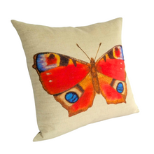 Load image into Gallery viewer, Peacock butterfly cushion in bright reds and blues against a neutral linen background viewed from the left side angle
